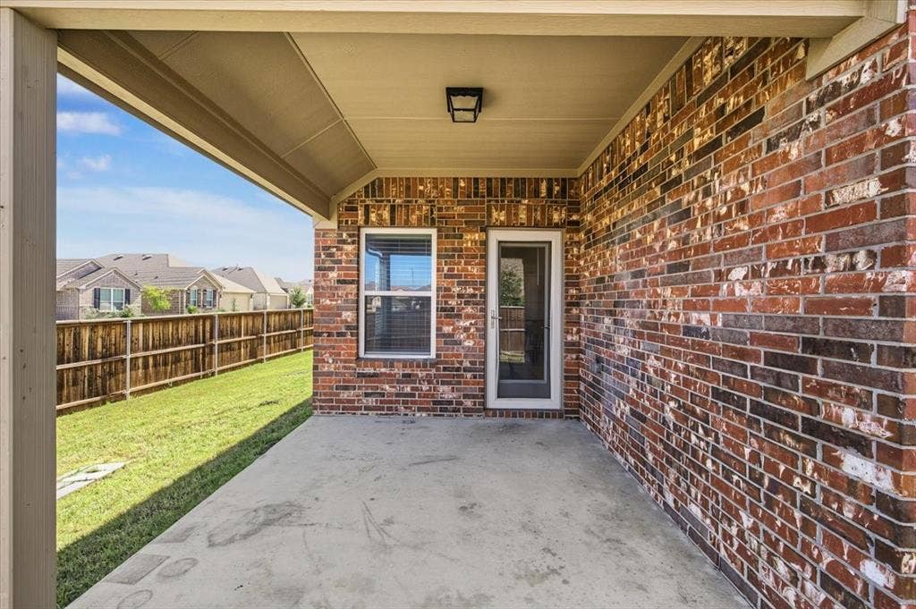 Covered concrete patio with a brick exterior wall, a glass-paneled door, and an exterior window
