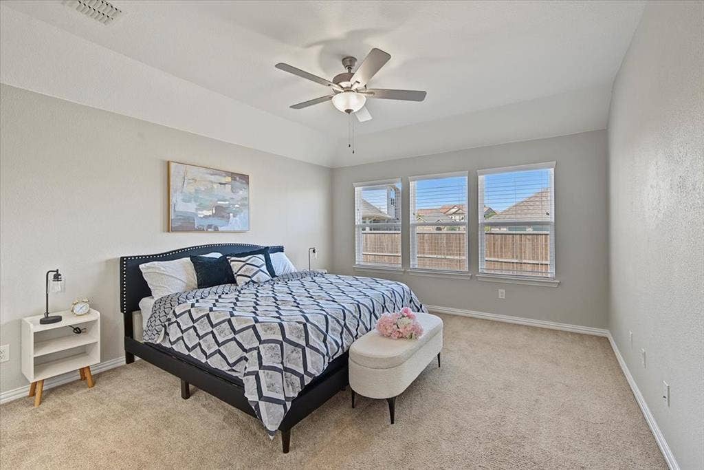 Tray ceiling with a ceiling fan and light fixture, three windows with blinds, and light-colored carpeting