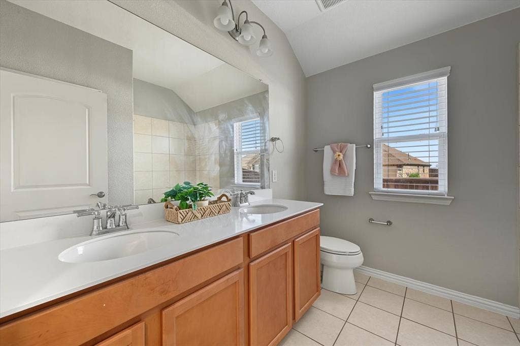 Dual vanity with integrated sinks and chrome fixtures, light wood-finish cabinetry, white countertop, and tiled flooring