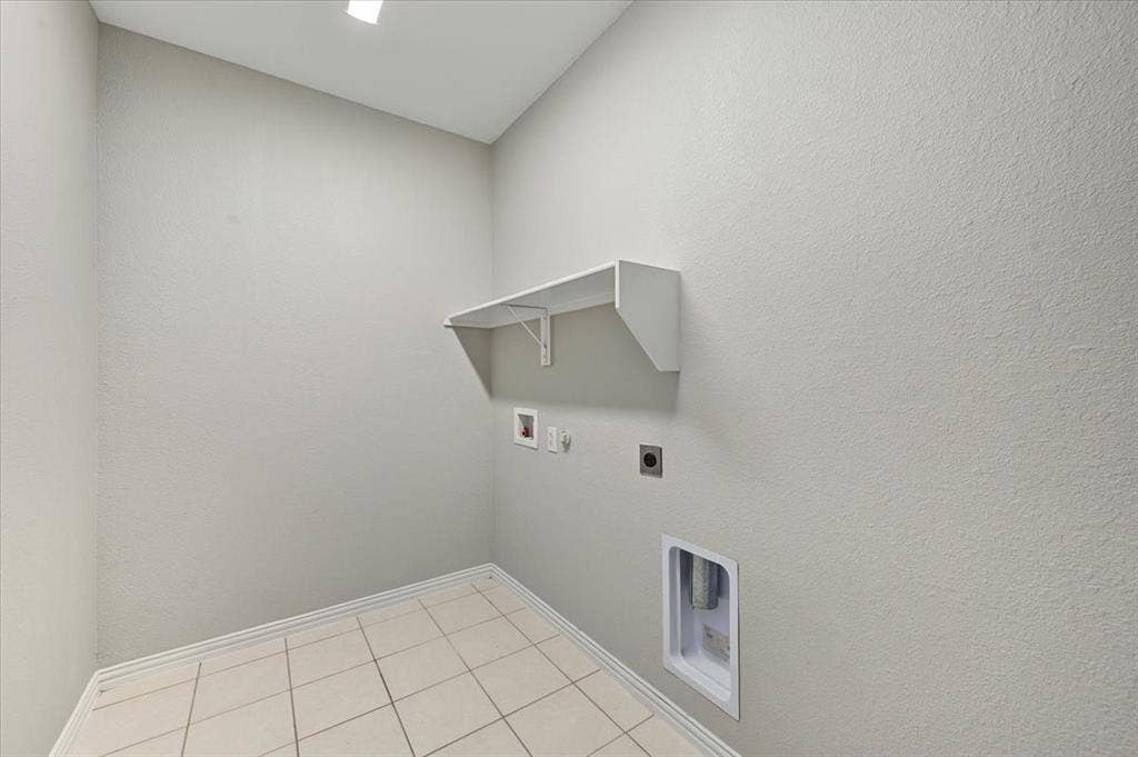 Light-toned walls with a wall-mounted shelf, tile flooring, and integrated laundry hookups