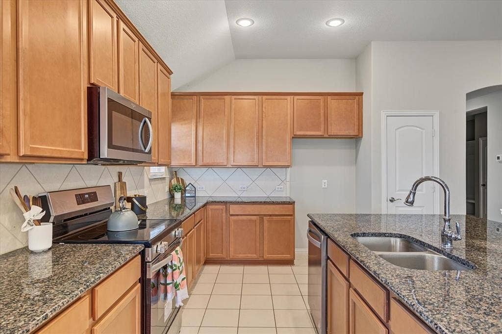 Kitchen featuring wood cabinetry, granite-style countertops, stainless steel appliances, a tile backsplash, and recessed lighting