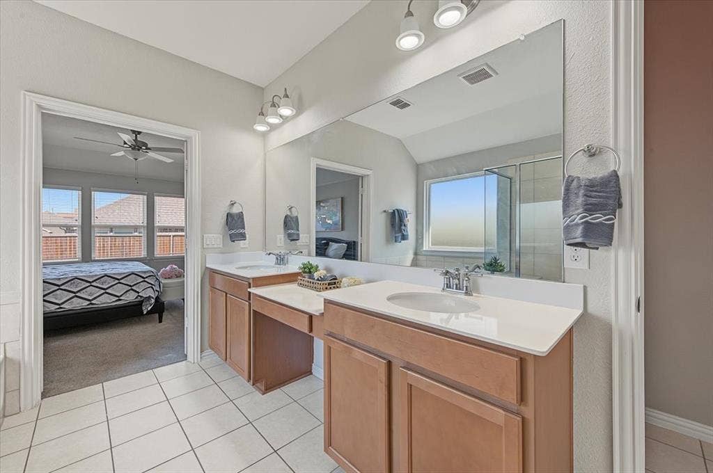 Dual vanities with integrated sinks and chrome fixtures, expansive mirror, wood-finish cabinetry, and tiled flooring