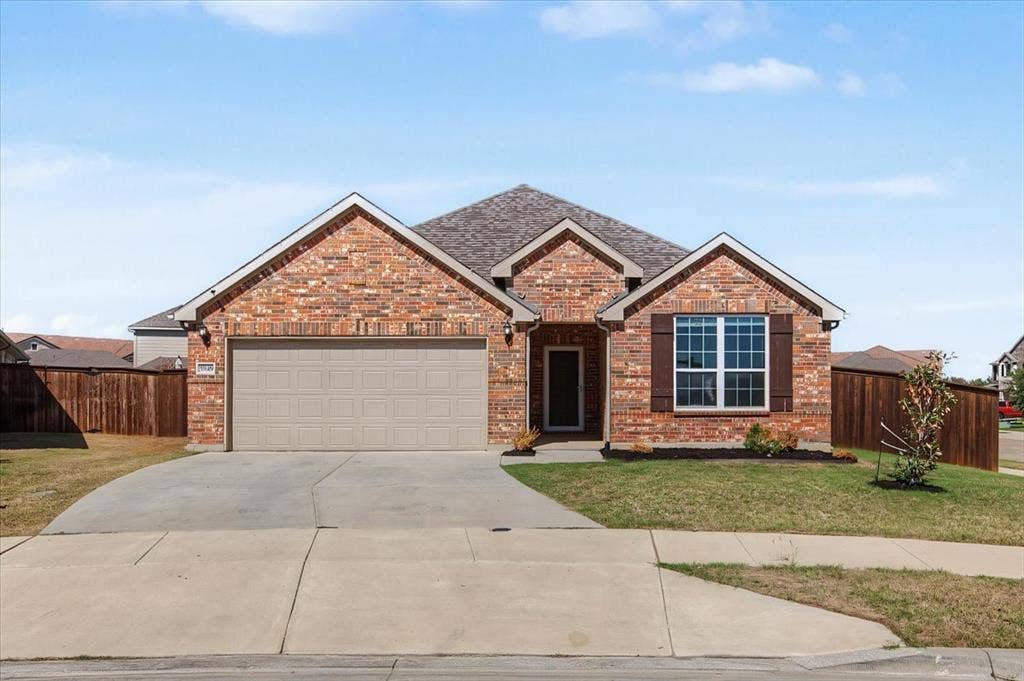 Brick exterior with contrasting brown shutters, an attached garage, a paved driveway, and manicured landscaping