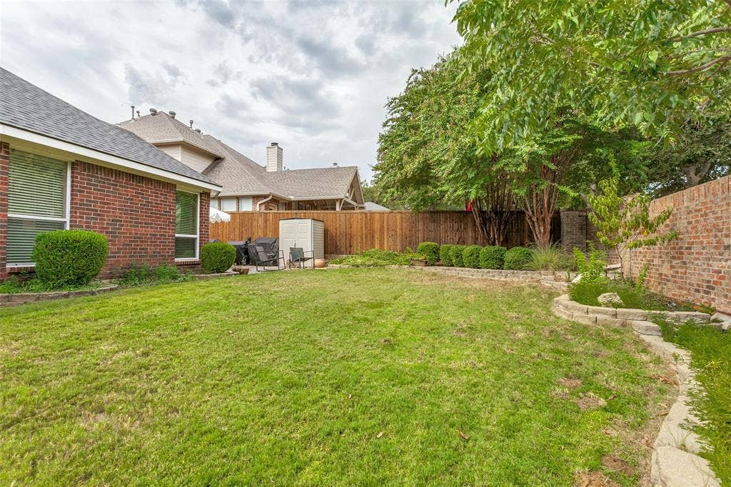Expansive backyard featuring a manicured lawn, wood fencing, and mature trees