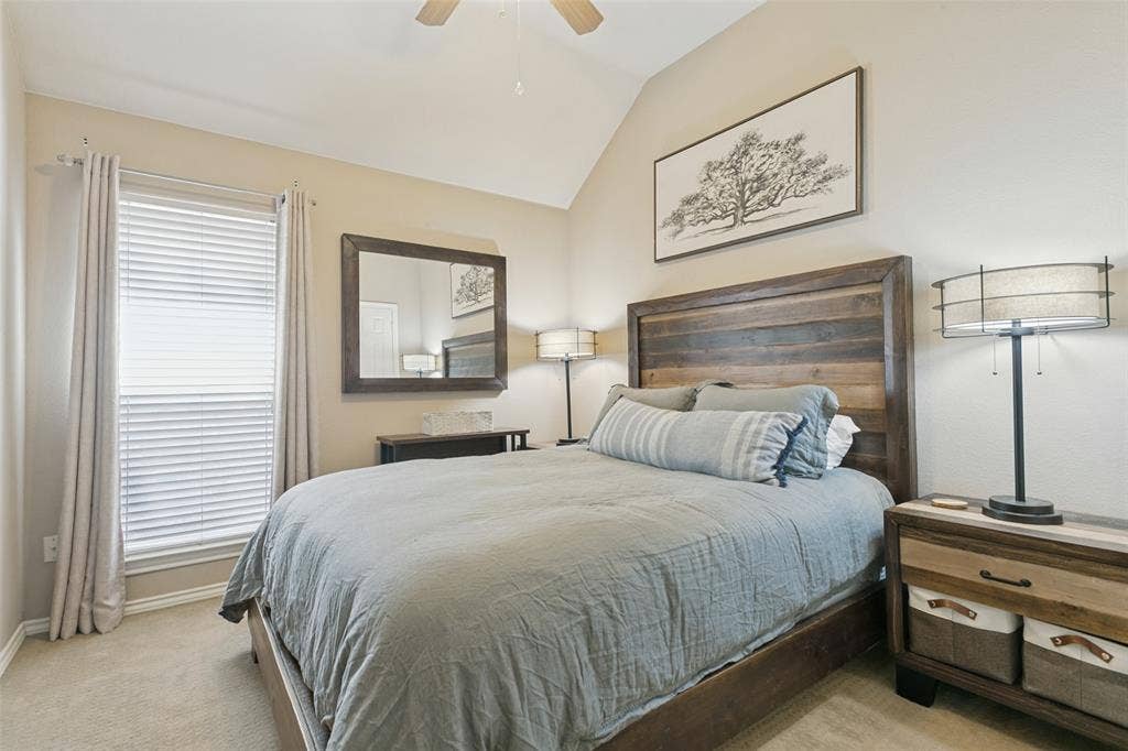 Vaulted ceiling with a ceiling fan, window with blinds, wood-finish headboard, and neutral carpeting