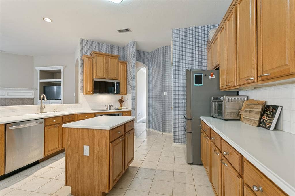 Kitchen featuring wood cabinetry, white countertops, tile flooring, a built-in microwave, and stainless steel appliances
