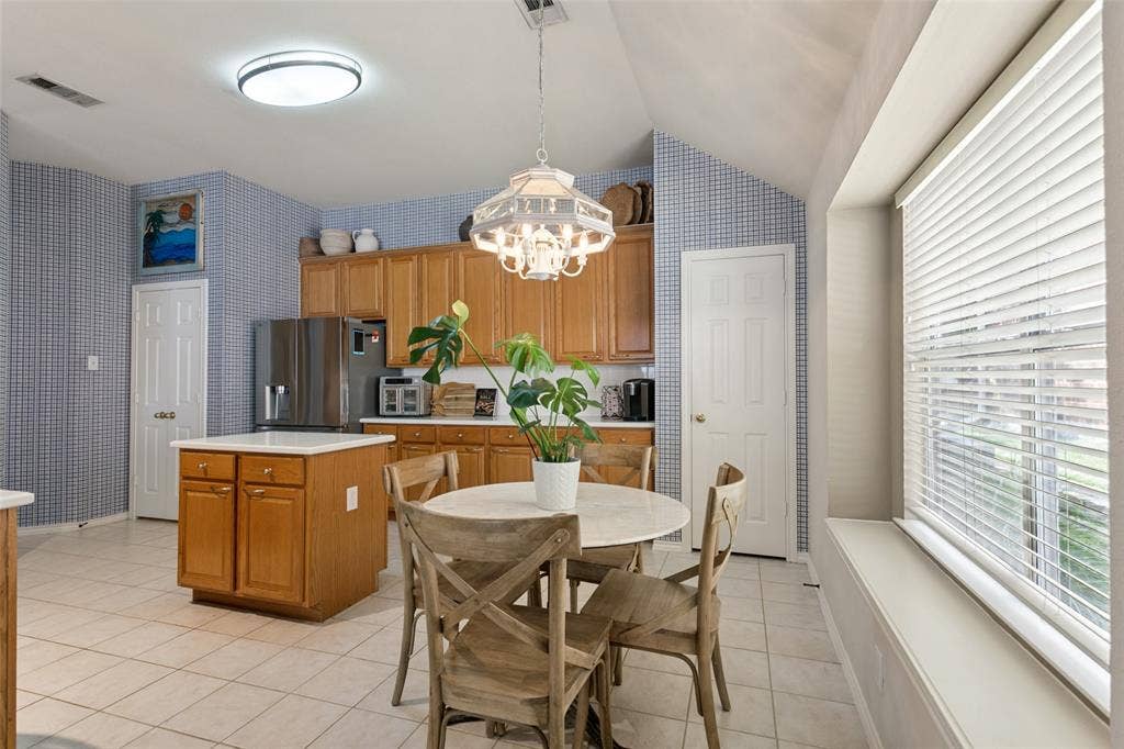 Kitchen space featuring a central island with white countertop, wood cabinetry, tile flooring, and a large window with blinds
