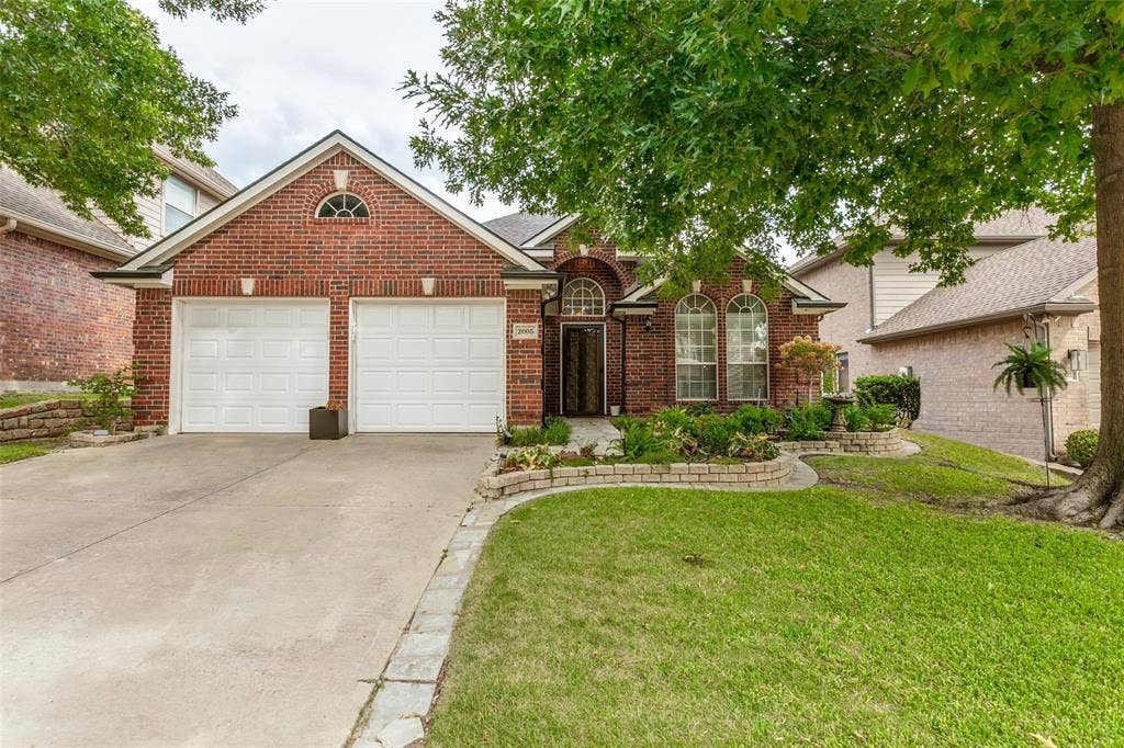Brick exterior with a two-car garage, concrete driveway, arched windows, and a landscaped front yard with stone-edged garden beds. House is on a cul-de-sac!