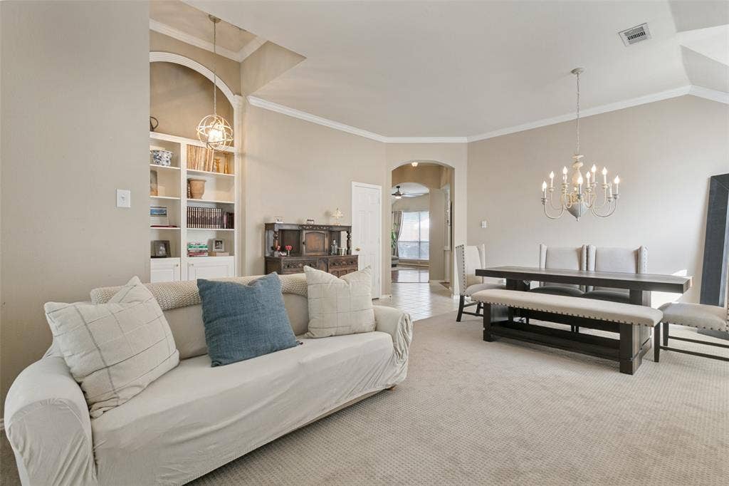 Built-in shelving with integrated lighting, vaulted ceiling, crown molding, arched entryways, and carpeted flooring