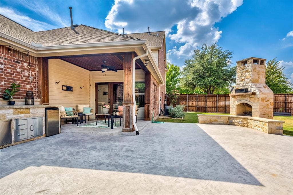 10138 Planters Row Drive, Frisco, TX 75033 The covered patio steps out to an extended patio anchored by a brick fireplace with wraparound stone-wall seating.