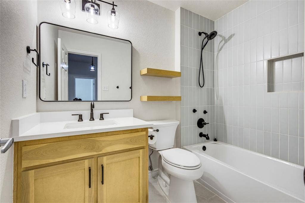 10138 Planters Row Drive, Frisco, TX 75033 The updated upstairs bath features a warm wood vanity, matte black fixtures, and a tiled tub-shower combo.