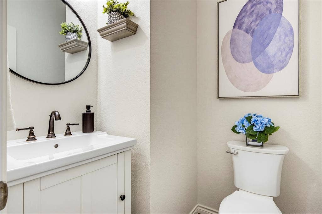10138 Planters Row Drive, Frisco, TX 75033 A stylish powder room with a round black mirror and modern fixtures, conveniently located on the main level for guests.