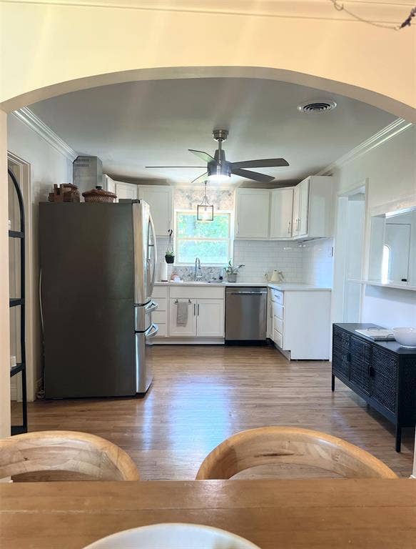 1200 Daisy Lane, Irving, TX 75061 Archway entry to kitchen featuring wood-finish flooring, white cabinetry, stainless steel appliances, and subway tile backsplash