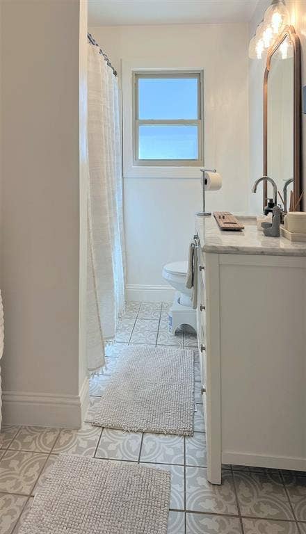 1200 Daisy Lane, Irving, TX 75061 Bathroom featuring a white vanity with a light-toned countertop, patterned floor tiling, a single window, and a wall-mounted light fixture above a mirror