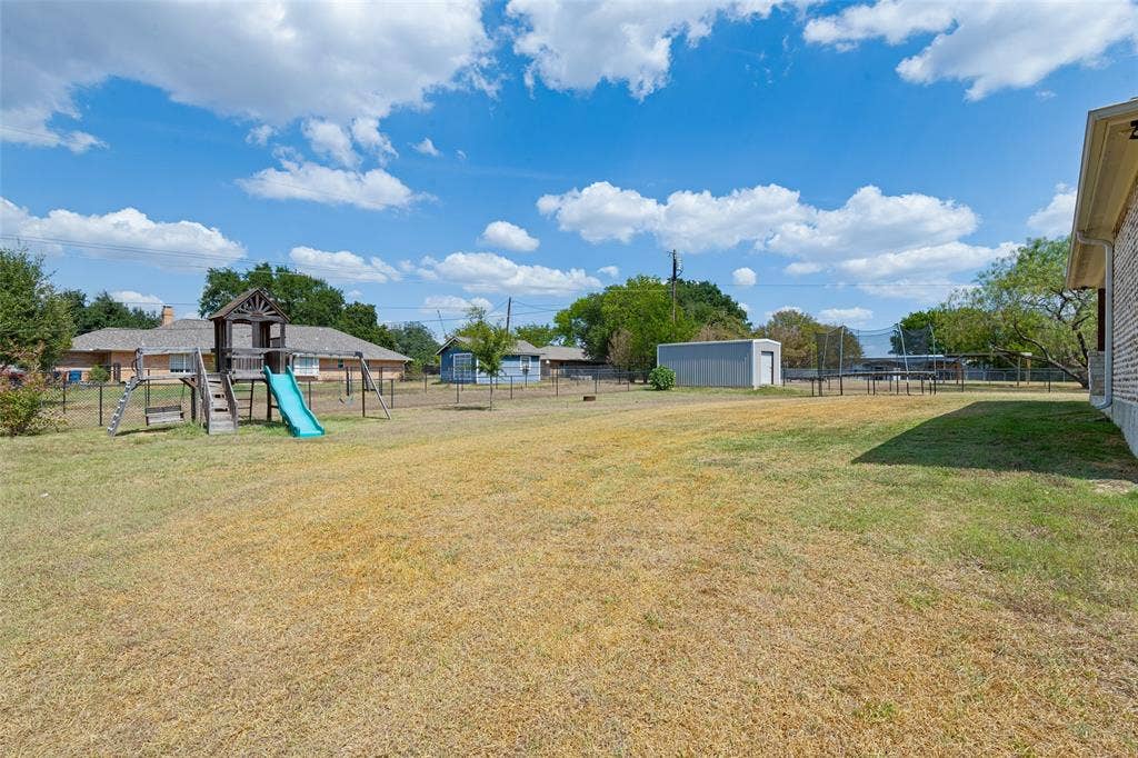 108 Rye Place, Gun Barrel City, TX 75156 Expansive backyard featuring a fenced perimeter, a wooden playset with a slide, and a detached storage shed