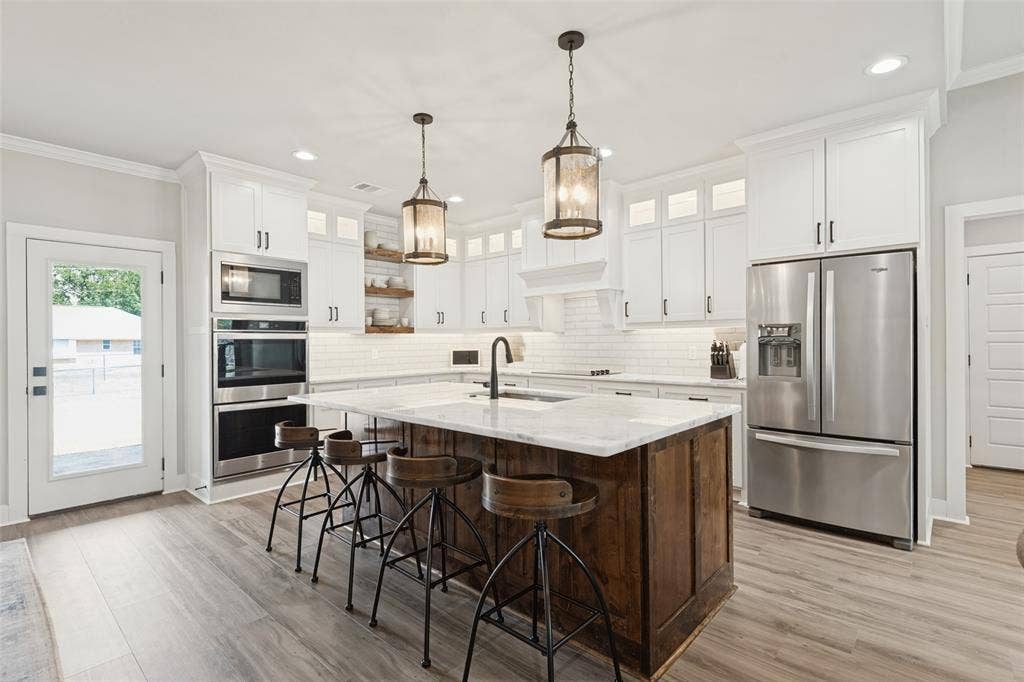 108 Rye Place, Gun Barrel City, TX 75156 Spacious kitchen featuring a wood-finish island with a light-toned countertop, white cabinetry with dark hardware, stainless steel appliances, and wood-finish flooring