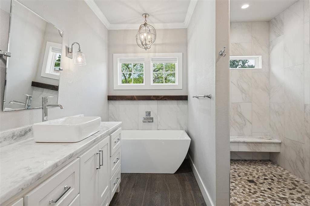 108 Rye Place, Gun Barrel City, TX 75156 Freestanding soaking tub, dual windows with wood trim, wood-finish flooring, white vanity with stone countertop, and a walk-in shower with pebble tile floor and built-in bench