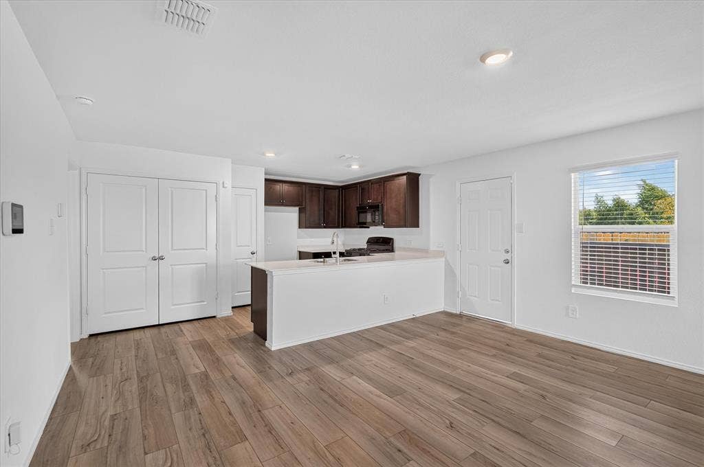 Open-concept kitchen and living area featuring wood-finish flooring, white walls, dark wood cabinetry, and a kitchen island with a white countertop