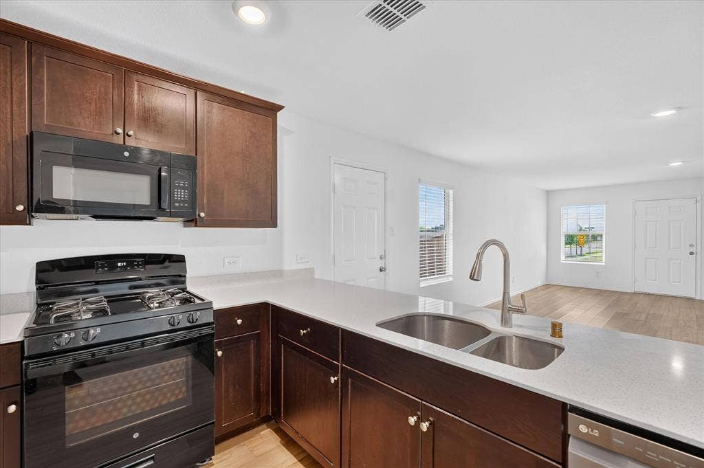 Kitchen featuring dark wood-finish cabinetry, light-toned countertops, a gas range, and a dual basin sink