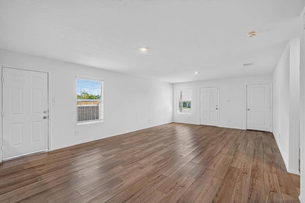Spacious room featuring wood-finish flooring, multiple windows with blinds, recessed lighting, and white paneled doors