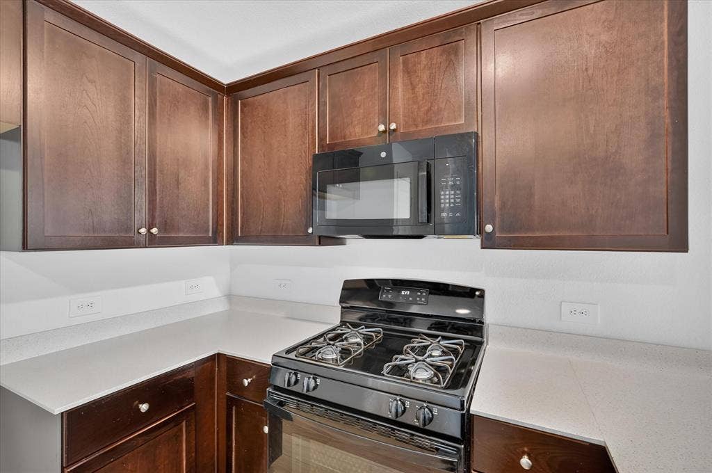Rich wood cabinetry, light-toned countertops, a built-in microwave, and a black range