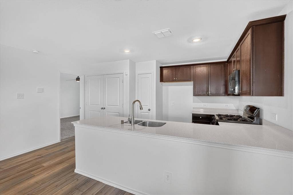 Kitchen featuring a gas range, dark wood-finish cabinetry, light-colored countertops, and a double-basin stainless steel sink with a gooseneck faucet