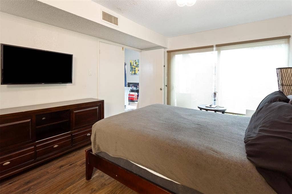 13026 Leader Street, #951, Houston, TX 77072 Bedroom 1 -Wood-finish flooring with a wall-mounted display, built-in media console, and large sliding glass door