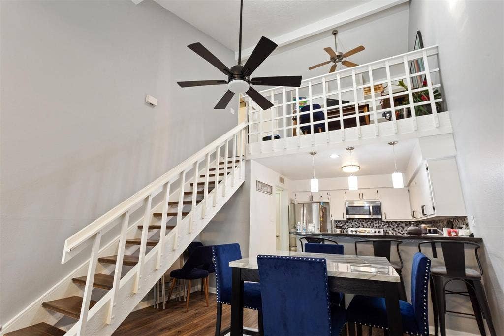 13026 Leader Street, #951, Houston, TX 77072 Vaulted ceiling with exposed beams, open loft area with white railing, kitchen featuring white cabinetry and stainless steel appliances, and wood-finish flooring