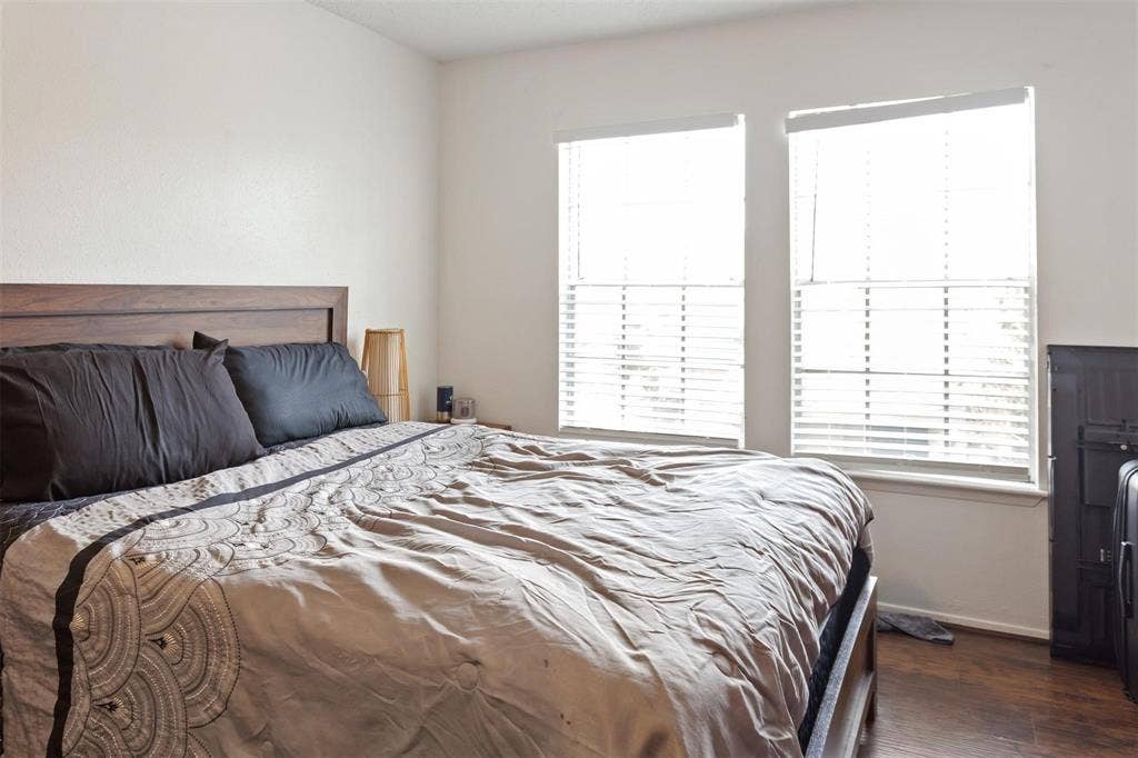 13026 Leader Street, #951, Houston, TX 77072 Bedroom 2 - Bright secondary bedroom featuring wood-finish flooring, plantation shutter-style window treatments, and abundant natural light from dual glass doors