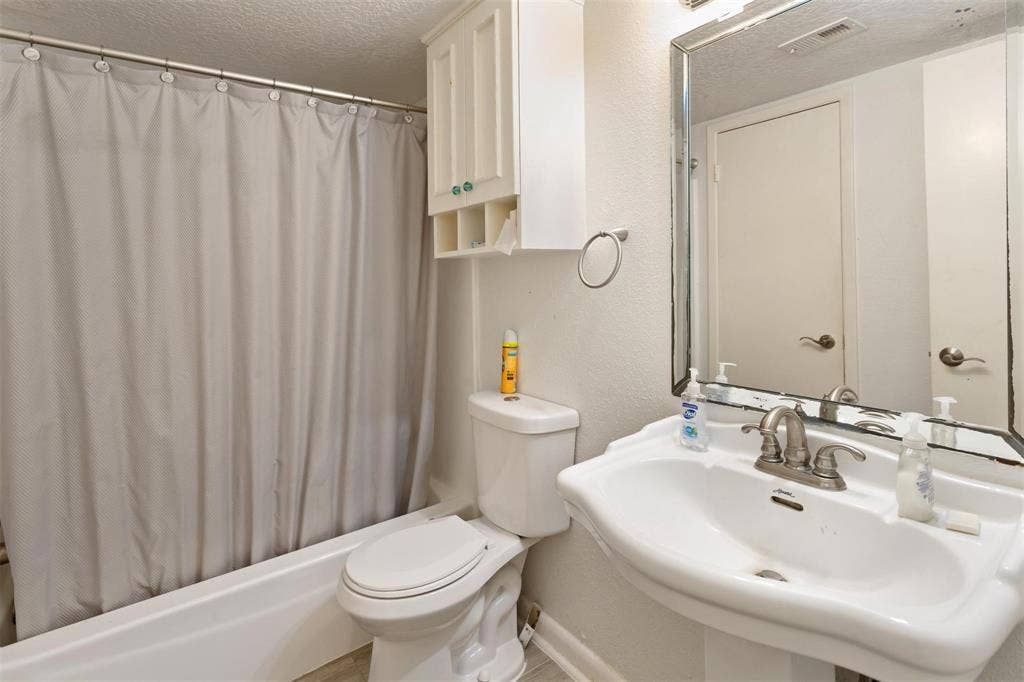 13026 Leader Street, #951, Houston, TX 77072 Bathroom 2 - Pedestal sink with a two-handle faucet, white bathtub with shower, and built-in upper cabinetry