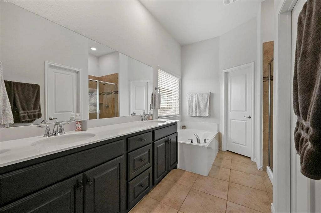 602 Brock Drive, Anna, TX 75409 Dual vanity with undermount sinks, built-in bathtub, separate glass-enclosed shower, expansive wall mirror, and tile flooring