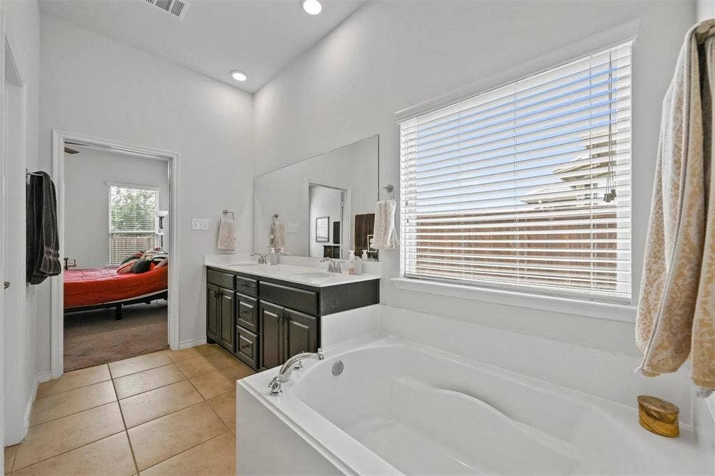 602 Brock Drive, Anna, TX 75409 Soaking tub with tile surround, dual vanity with undermount sinks, large wall-mounted mirror, and recessed lighting