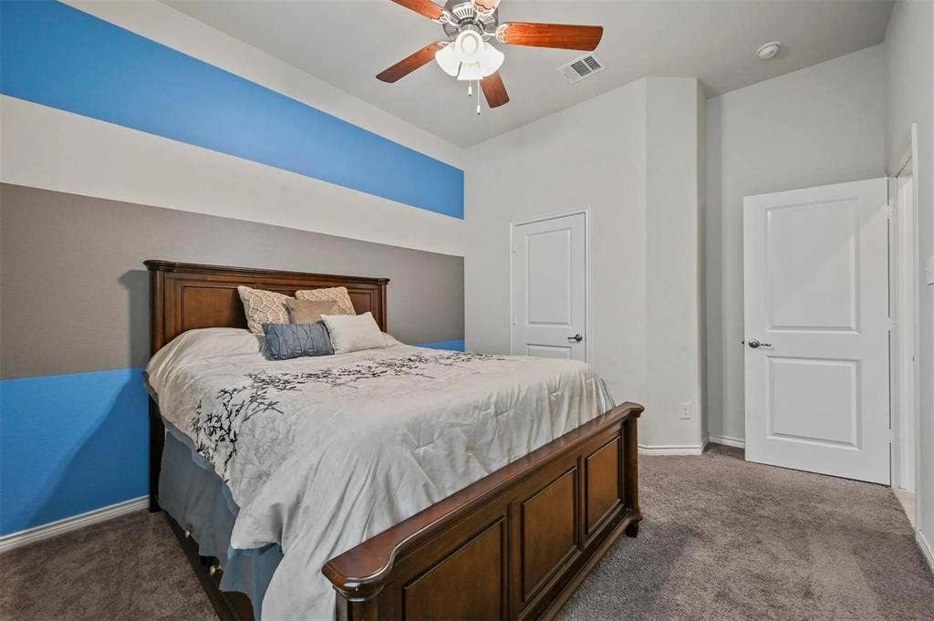 602 Brock Drive, Anna, TX 75409 Carpeted room featuring a ceiling fan with wood-finish blades, two panel doors, and a wall with a decorative stripe design