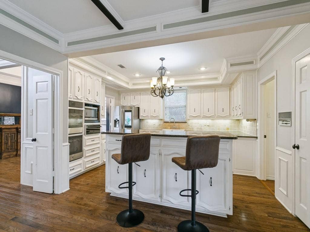 3309 Wolfe Court, Plano, TX 75025 Hardwood flooring with white cabinetry, stainless steel appliances, and a central island with a dark countertop