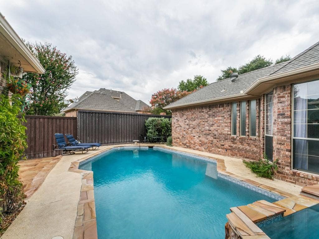 3309 Wolfe Court, Plano, TX 75025 Private backyard featuring a rectangular swimming pool with integrated spa, stone coping, and a full brick exterior