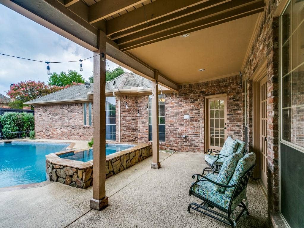 3309 Wolfe Court, Plano, TX 75025 Covered patio featuring an exposed aggregate concrete surface, brick exterior, and a built-in spa with stone surround