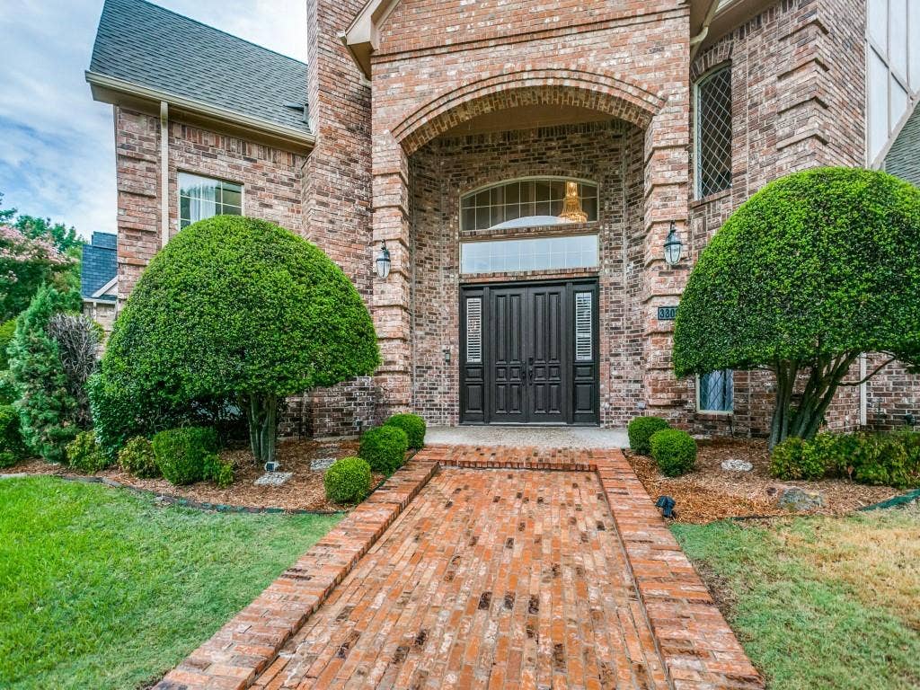 3309 Wolfe Court, Plano, TX 75025 Brick exterior with an arched entryway, double entry doors, brick paver walkway, and manicured shrubbery