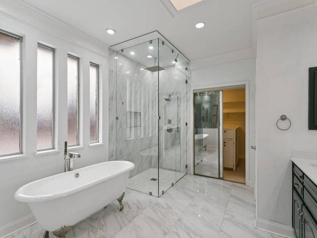 3309 Wolfe Court, Plano, TX 75025 Freestanding clawfoot tub with chrome fixtures, glass-enclosed shower with tiled walls and recessed lighting, marble-finish floor tiles, and a vanity with a white countertop and dark cabinetry