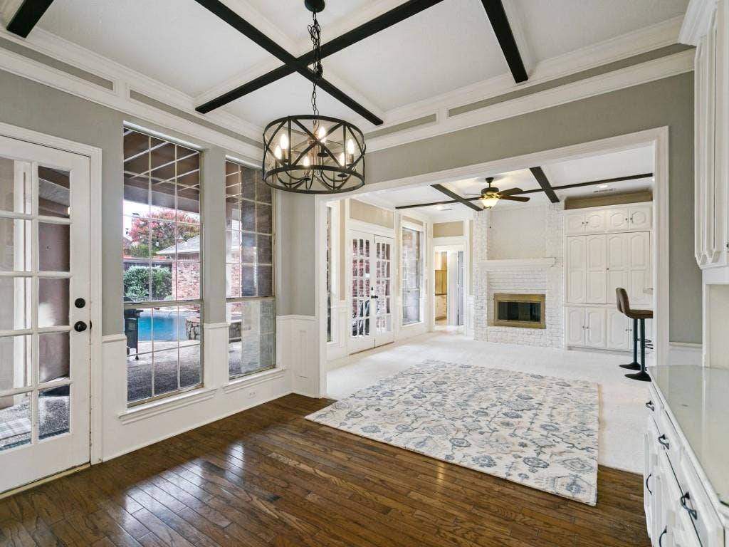 3309 Wolfe Court, Plano, TX 75025 Hardwood flooring, painted coffered ceiling, modern chandelier, double French doors, and a brick fireplace