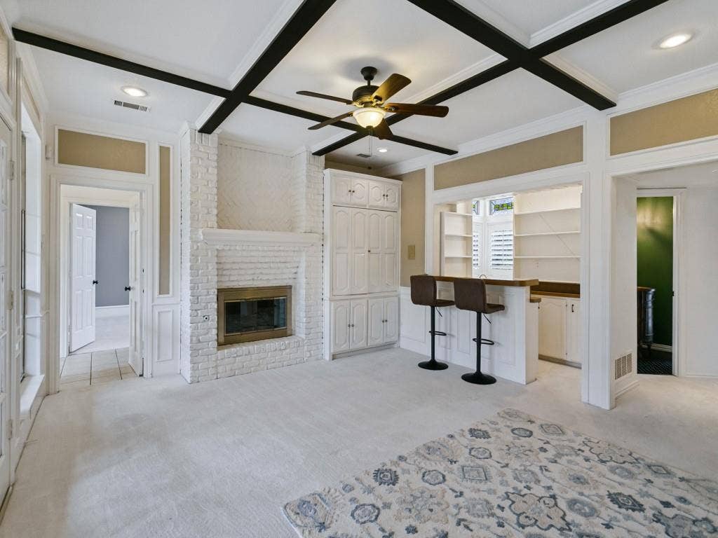 3309 Wolfe Court, Plano, TX 75025 Spacious primary suite featuring coffered ceiling with black wood beams, gas fireplace with white subway tile surround, built-in cabinetry with shaker-style doors, quartz countertop wet bar with seating for two, and light wood-finish flooring throughout