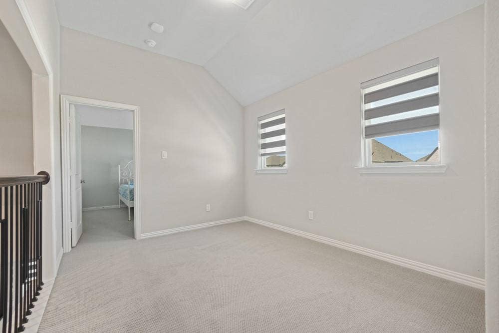 Vaulted ceiling, two windows with blinds, light-toned carpeting, and a doorway