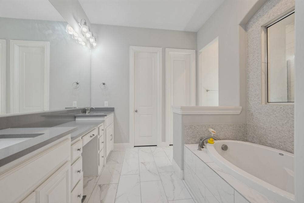 Dual vanity with integrated sinks, extensive counter space, white cabinetry, a separate soaking tub, and tile flooring