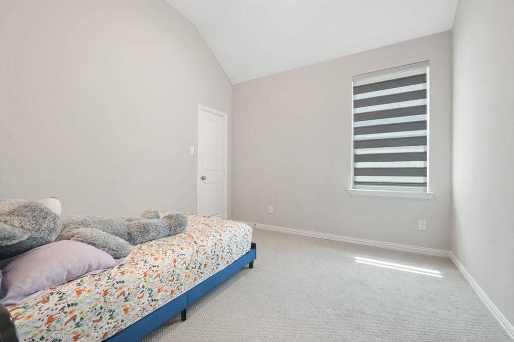 Vaulted ceiling with neutral wall tones, window with horizontal blinds, and light-colored carpet flooring