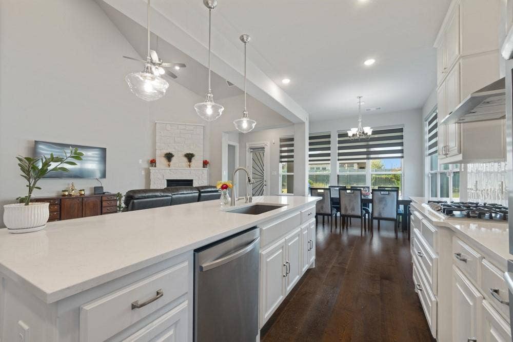 Open-concept kitchen featuring an island with a built-in sink, white cabinetry with silver hardware, stainless steel appliances, and dark wood-finish flooring