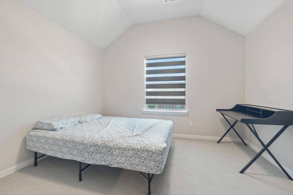 Vaulted ceiling, neutral tone walls, carpeted flooring, and a window with horizontal blinds