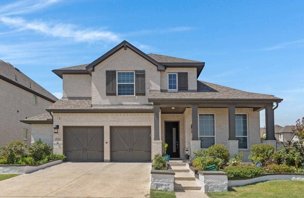 Two-story exterior featuring a covered porch, two-car garage, and stone-accented landscaping