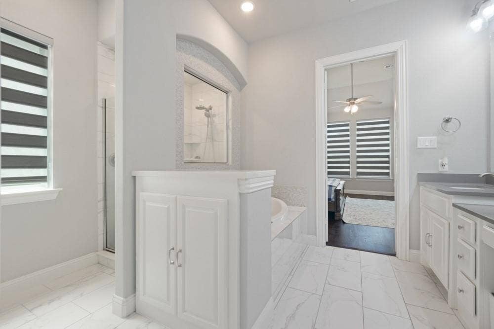 Spacious bathroom featuring a built-in soaking tub, a separate glass-enclosed shower, dual vanities with integrated sinks, white cabinetry, and large format tile flooring