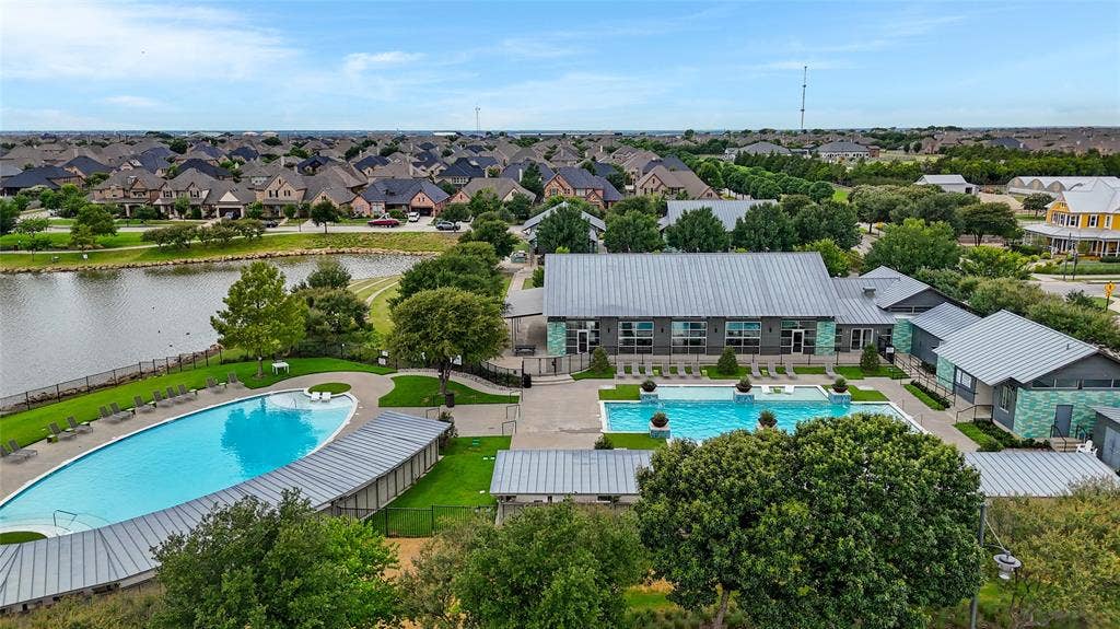 Lakeside community featuring two swimming pools, a central amenity building with a metal roof, and surrounding residential properties