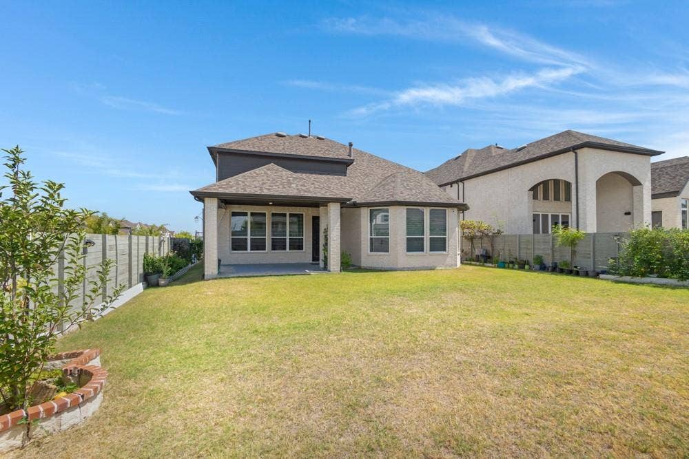 Expansive backyard with a covered patio, concrete fencing, and a bay window