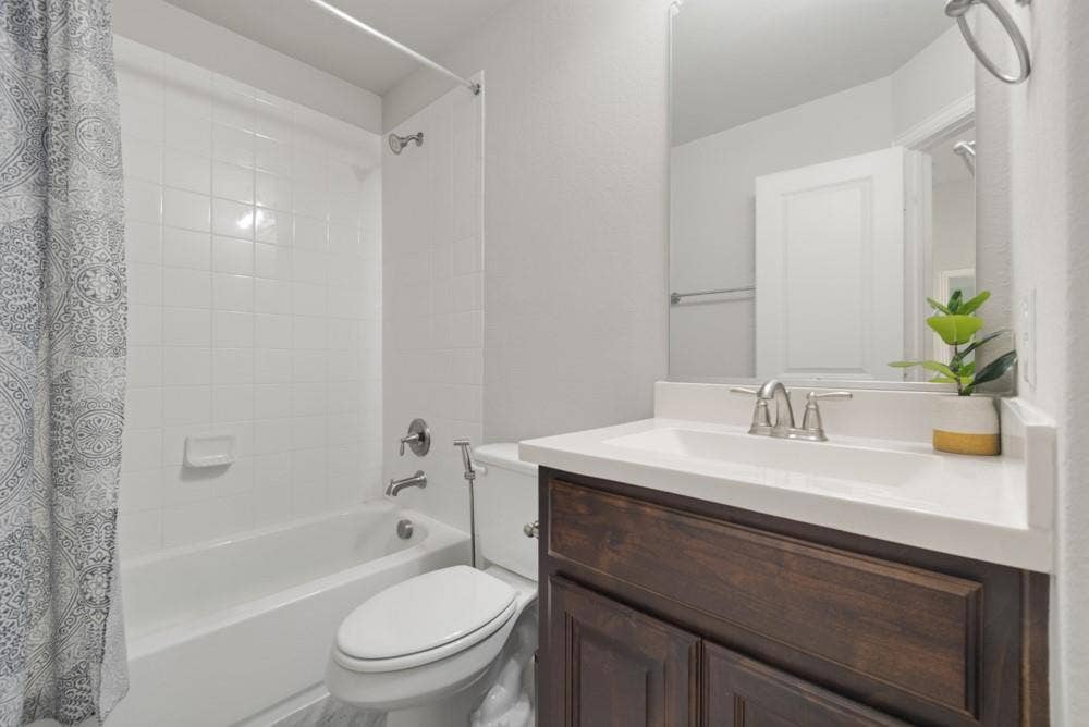 Bathroom featuring a tub and shower combination with white tile surround, a dark wood-finish vanity, an integrated sink with a light-colored countertop, and a wall-mounted mirror